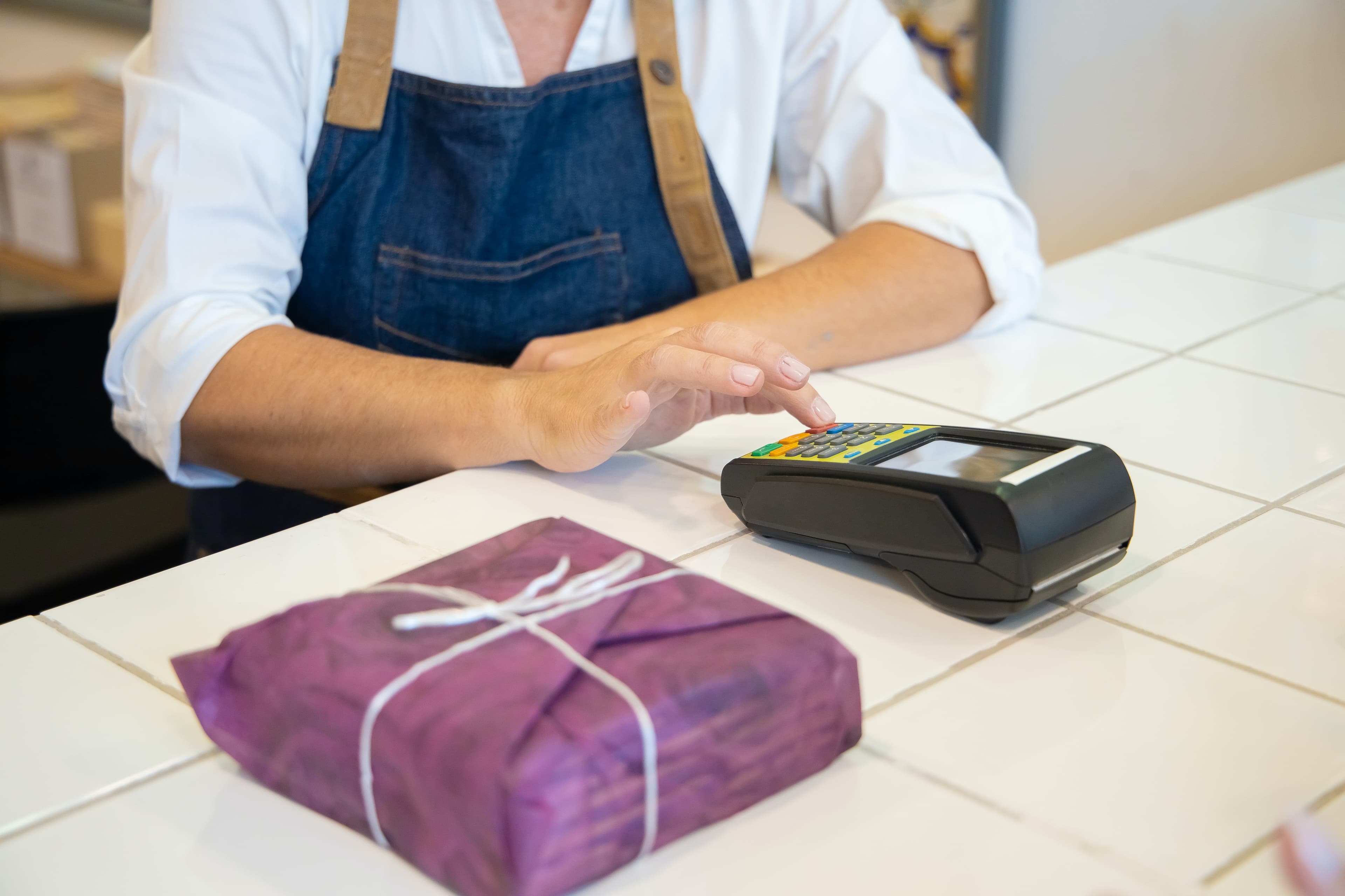 A shop worker entering a payment on a card terminal beside a wrapped parcel